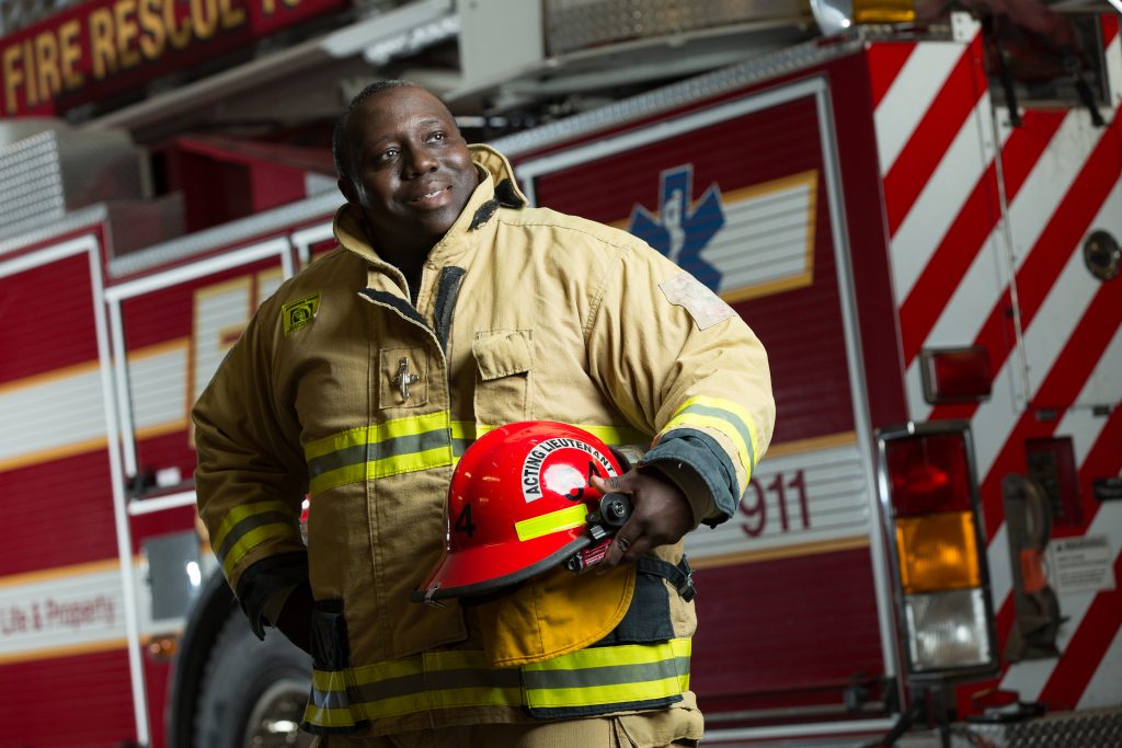 Middle aged man in full fire fighter uniform standing in front of fire engine